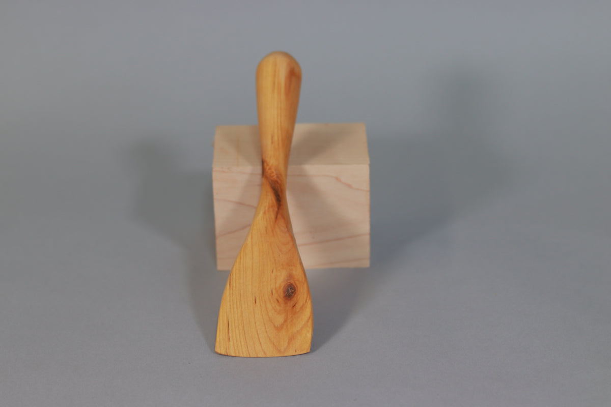 A spatula made of birch wood shown against a gray background. A small knot near the right edge of the blade.