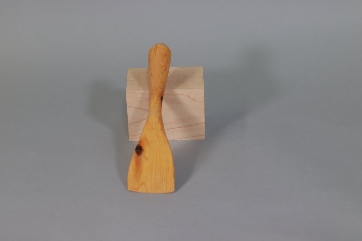 A white birch spatula against a grey background. Dark colored knot on left edge of blade.