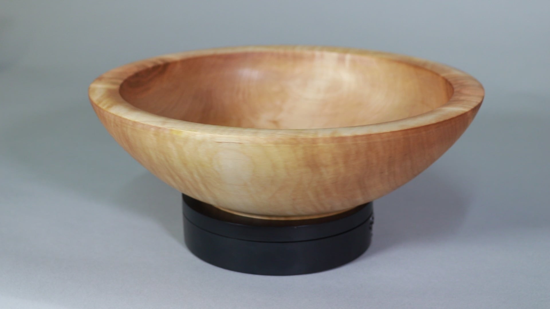 a medium sized maple salad bowl with an ogee shaped base is rotating on a small black turntable