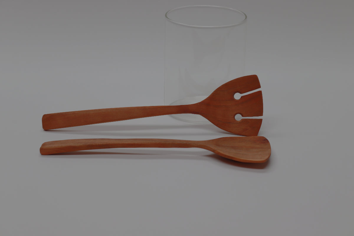 a pair of cherry salad servers, 10 inches long and 3 inches wide at the business end, lie horizontally in front of a white background.