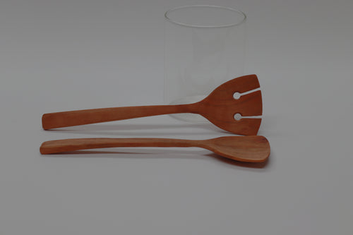 a pair of cherry salad servers, 10 inches long and 3 inches wide at the business end, lie horizontally in front of a white background.
