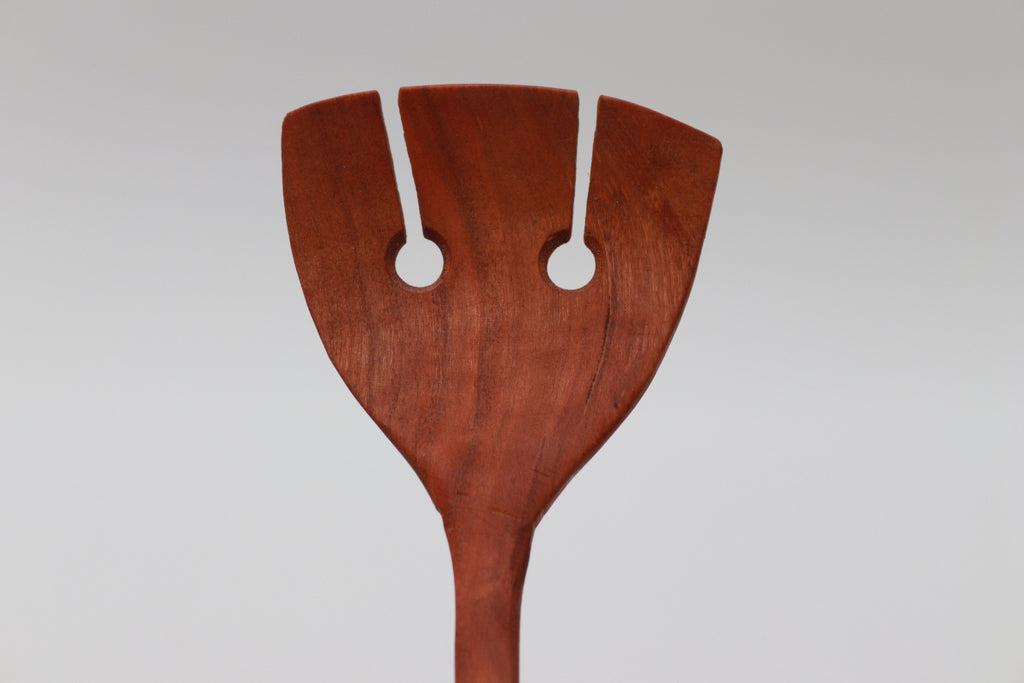 A cherry salad server, looking a bit like a spatula with its two cutouts, in front of a white background.