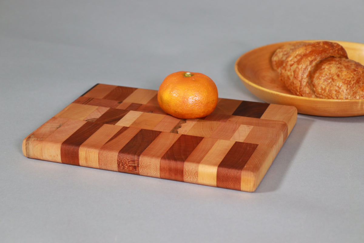 wooden end grain cutting board with tangerine and croissant for scale. board is maple, cherry, and walnut