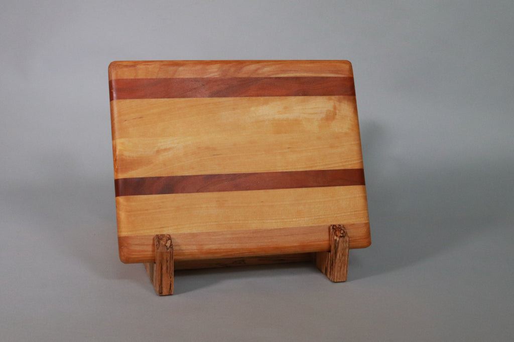 Wooden cutting board laminated from contrasting strips of hardwood on a stand in front of a gray background