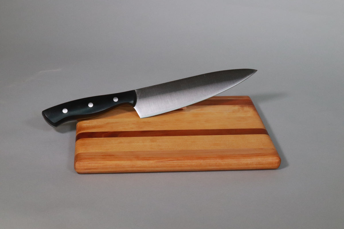 Standard 8 inch chef's knife on a laminated wooden cutting board against a gray background. This big kitchen knife is too big for most of the work you would do on this board, but it shows the scale of the board so you aren't disappointed with how small it is when it arrives.